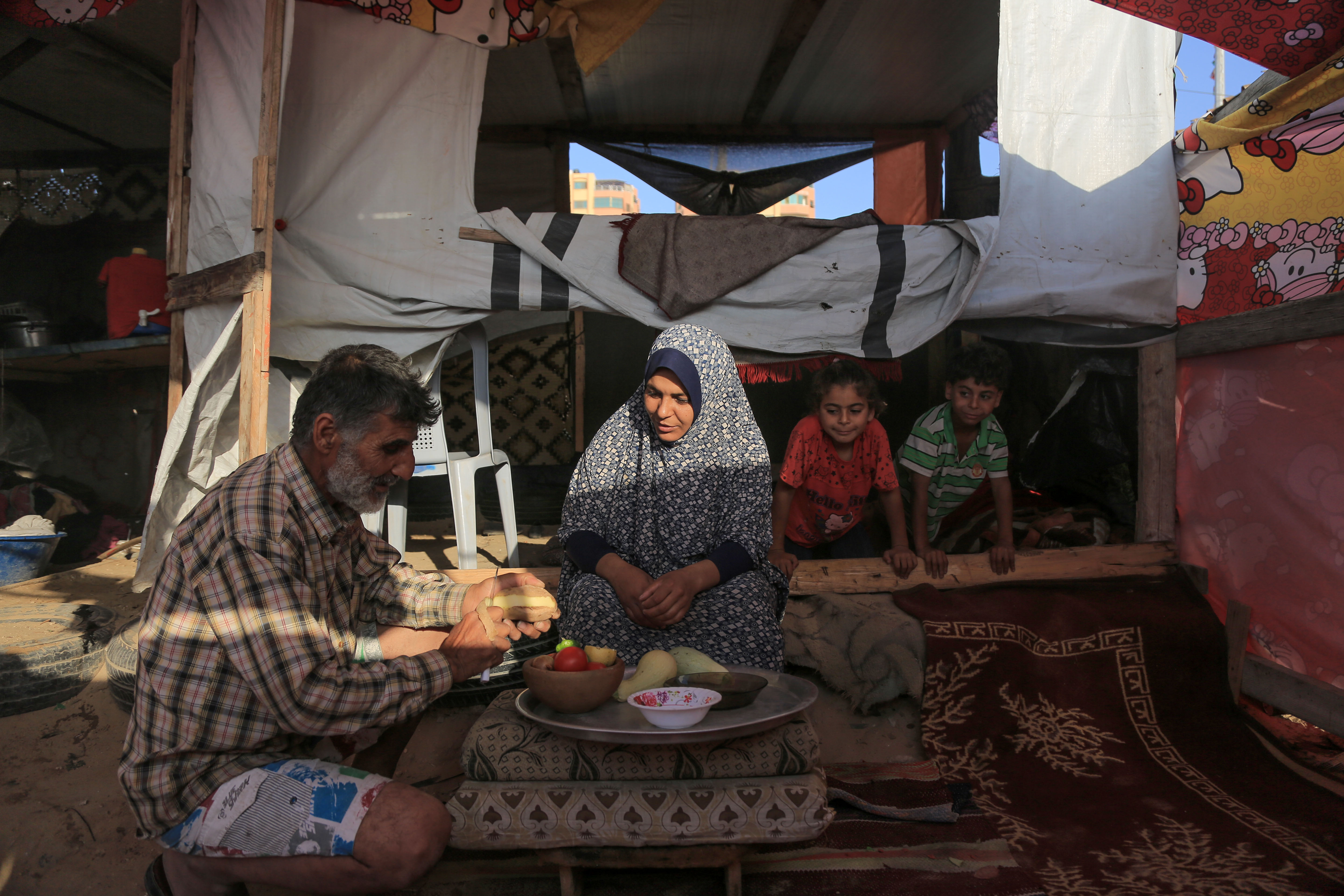 Hani peels a potato to be sliced and fried for the upcoming iftar meal as Malak and Ahmad watch with anticipation.