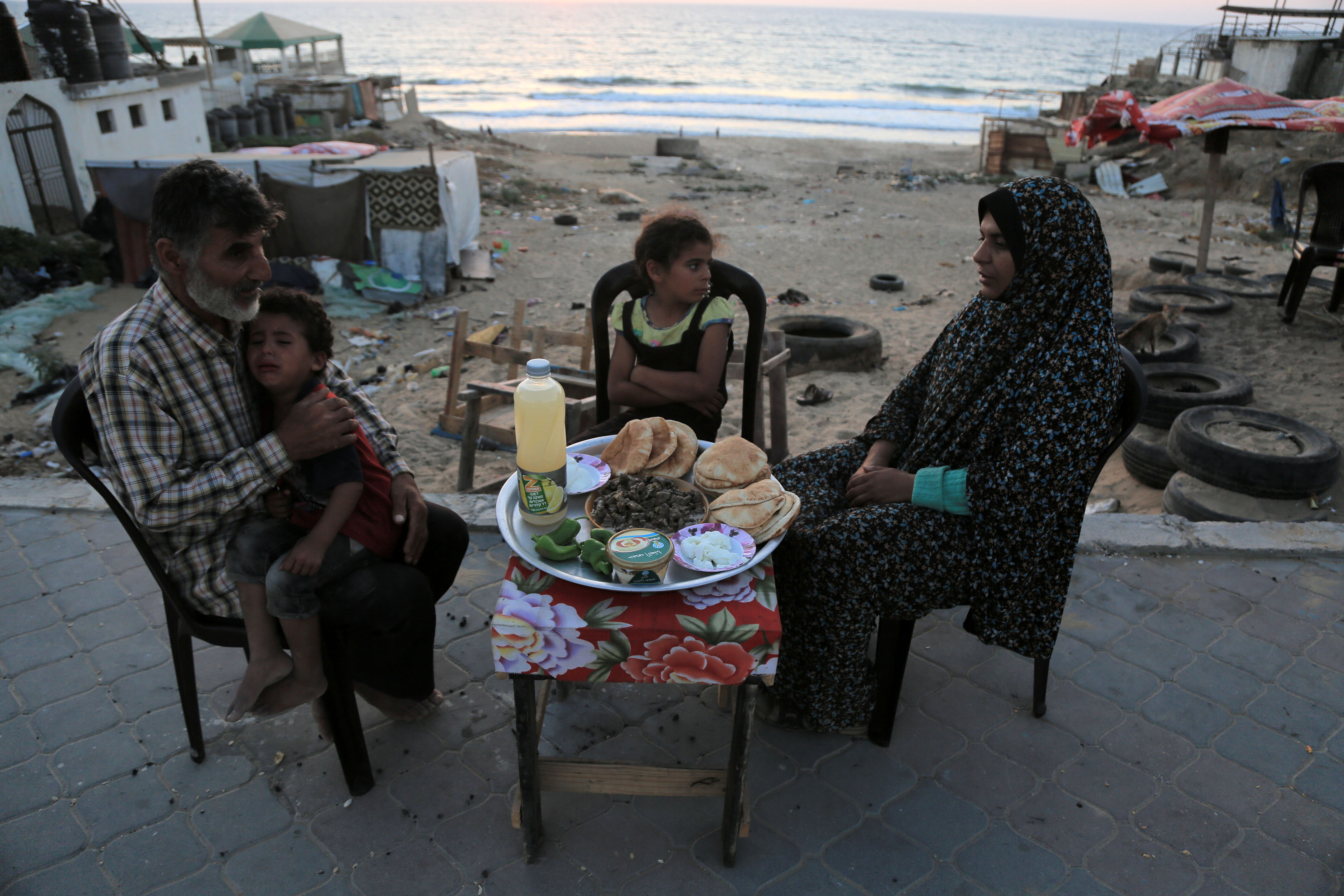 The al-Lahham family gathers for iftar (the meal that breaks the daily Ramadan fast) on the beach front sidewalk outside the tent where they live. The daily iftar ritual helps the family to preserve some sense of normalcy.