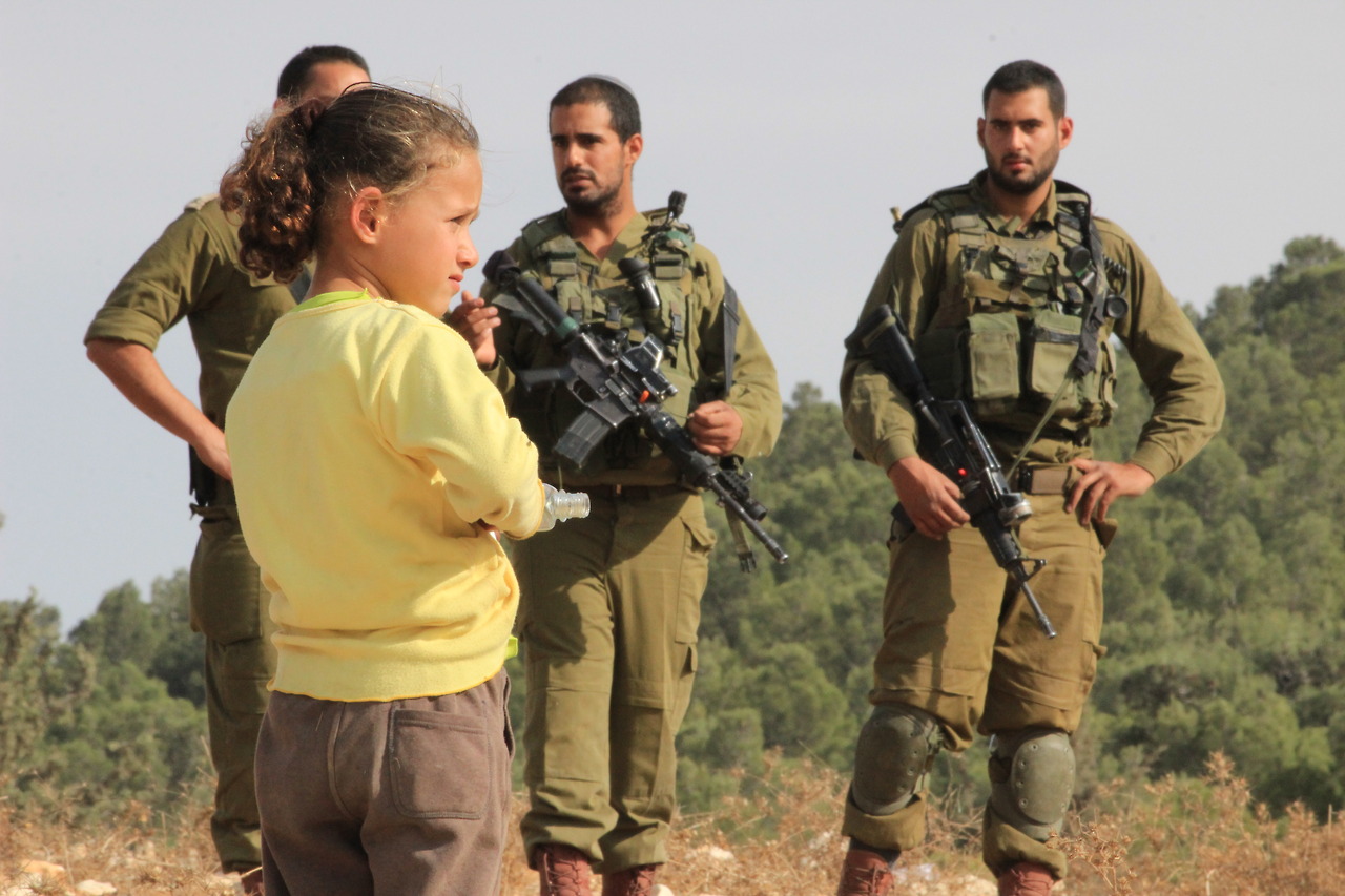 A Palestinian girl from At-Tuwani stands in front of Israeli soldiers.
