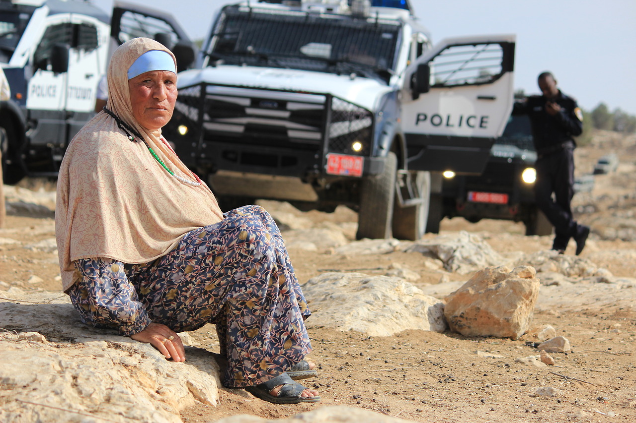 A Palestinian woman from At-Tawani with Israeli police and military vehicles in the background.
